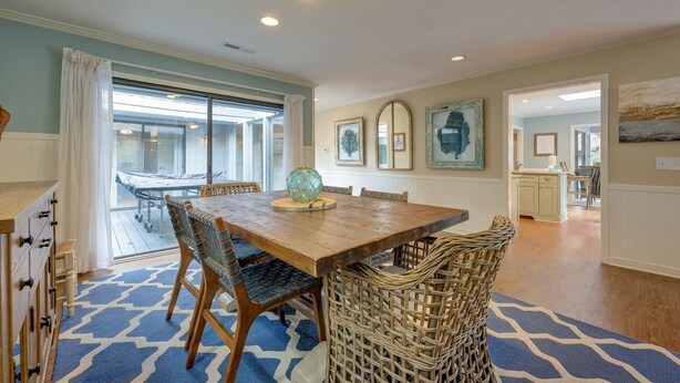 A dining area with a wooden table and wicker chairs, a blue patterned rug, and a view of the outdoor patio through a glass door.