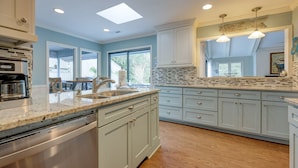 A modern kitchen with light blue cabinets, a large island with a sink, and a backsplash with a mosaic tile pattern.