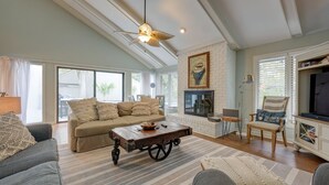 A spacious living room with a high ceiling, a fireplace, and a large window.