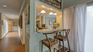 A kitchen with a bar area, wooden chairs, and a large window with sheer curtains.
