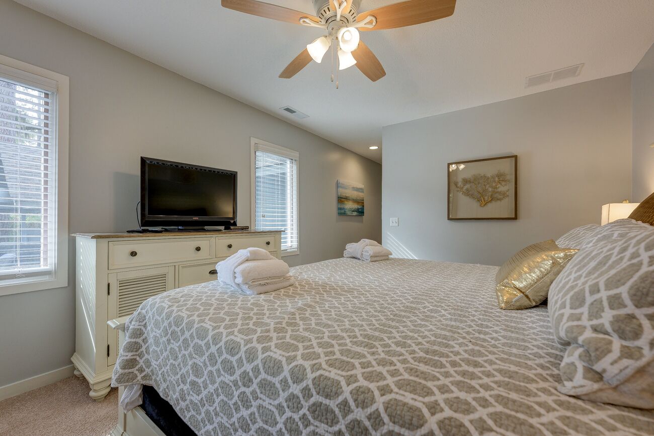 A bedroom with a bed, a television on a dresser, and a ceiling fan.