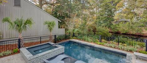 A swimming pool with a hot tub, surrounded by a wooden deck and a metal fence.