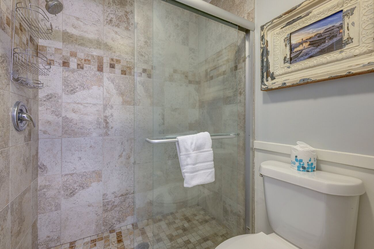 Une salle de bain avec une douche à parois de verre, des toilettes blanches et un porte-serviettes.