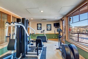 A gym with various exercise equipment, a television, and a view of a snowy landscape through large windows.