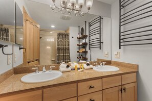 A modern bathroom with two sinks, wooden cabinets, a large mirror, and a towel rack.