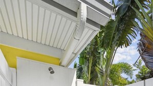 A white gate with a metal handle, a yellow wall, and a tiled patio area. - Holmes Beach Cottage Steps to the Beach with Heated Pool! (Holmes Beach)