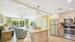 A modern kitchen with a central island, stainless steel appliances, and a dining area with a sofa and chairs. - Holmes Beach Cottage Steps to the Beach with Heated Pool! (Holmes Beach)