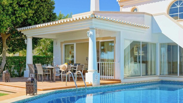 Ein Poolbereich mit überdachter Terrasse, Gartenmöbeln und freiem Blick auf den Pool.