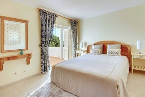 Ein Schlafzimmer mit Bett, Nachttischen, Fenster mit Vorhängen, einem gerahmten Bild und Blick ins Freie.