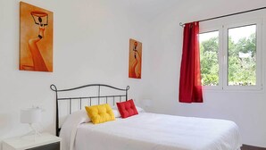 A bedroom with a bed, a nightstand, a window with red curtains, and two paintings on the wall.