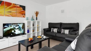 A modern living room with a black sofa, a coffee table, a flat-screen TV, a white shelving unit, and a large floral artwork.