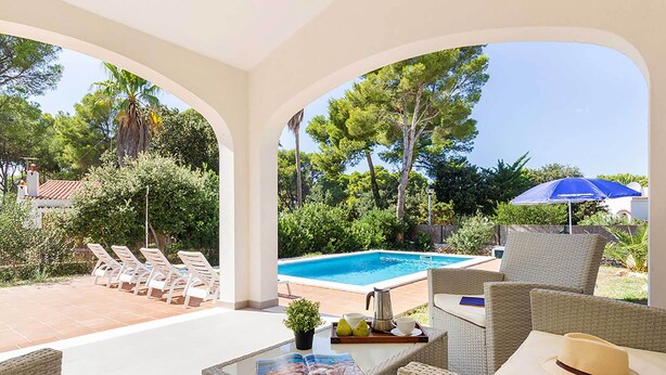 A covered outdoor area with wicker furniture, a pool, and a view of the surrounding greenery.