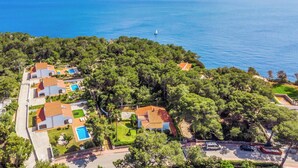 An aerial view of a coastal property with multiple villas, a swimming pool, and a lighthouse in the distance.