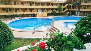 En swimmingpool omgivet af en blomsterfuld have med en fleretasagers bygning i baggrunden.