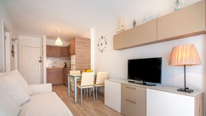 En moderne, kompakt opholdsstue med tekøkken, spiseplads og TV.