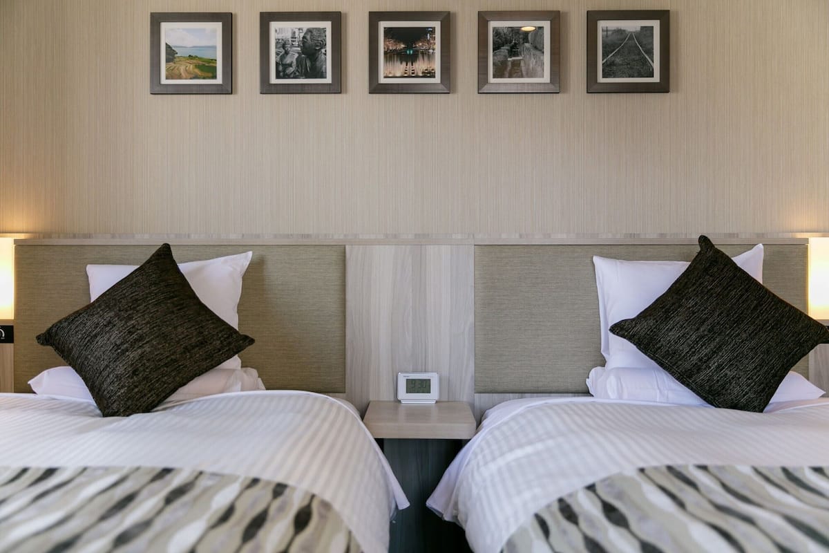 Een hotelkamer met twee bedden, elk voorzien van een kussen en een nachtkastje met een wekker.