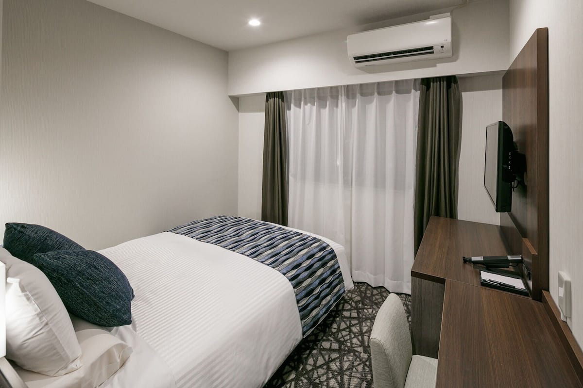 Een hotelkamer met een bed, een bureau, een televisie en een airconditioning.