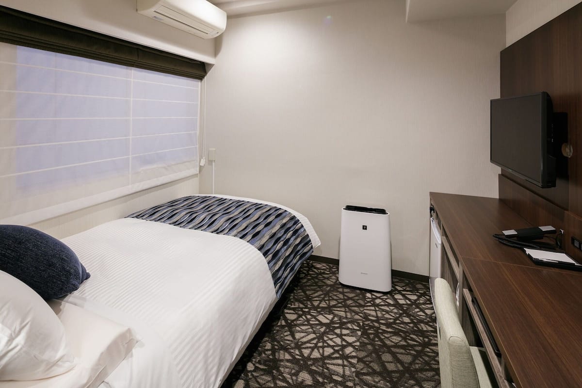 Een hotelkamer met een bed, een bureau, een televisietoestel en een airconditioner.