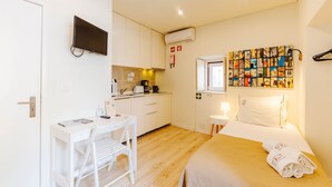 Una habitación de hotel pequeña con cama, escritorio, silla, televisor y kitchenette.