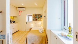 Una habitación compacta con cama, una kitchenette pequeña, una ventana con vistas y una pared decorada con una obra de arte colorida.