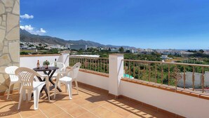A balcony with a table and chairs, a view of a cityscape and mountains, and a clear blue sky. - Villa Jara - Three Bedroom Villa, Sleeps 6 (Nerja)