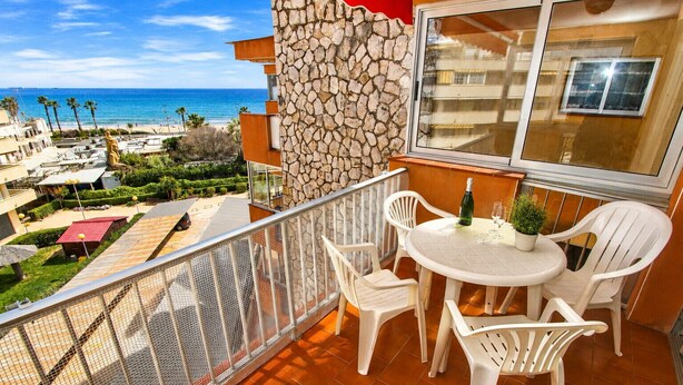 A balcony with a view of the sea, white plastic chairs, a table with a bottle and glasses, and a stone wall. - DMS Apartment (La Pineda)
