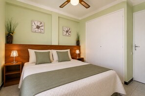 A neatly arranged bedroom with a bed, two bedside lamps, a wooden headboard, and two wall-mounted flower paintings.