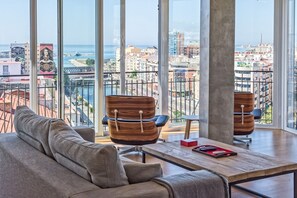 Una sala de estar moderna con un ventanal grande que da a una vista panorámica de la ciudad, incluyendo un río y edificios.