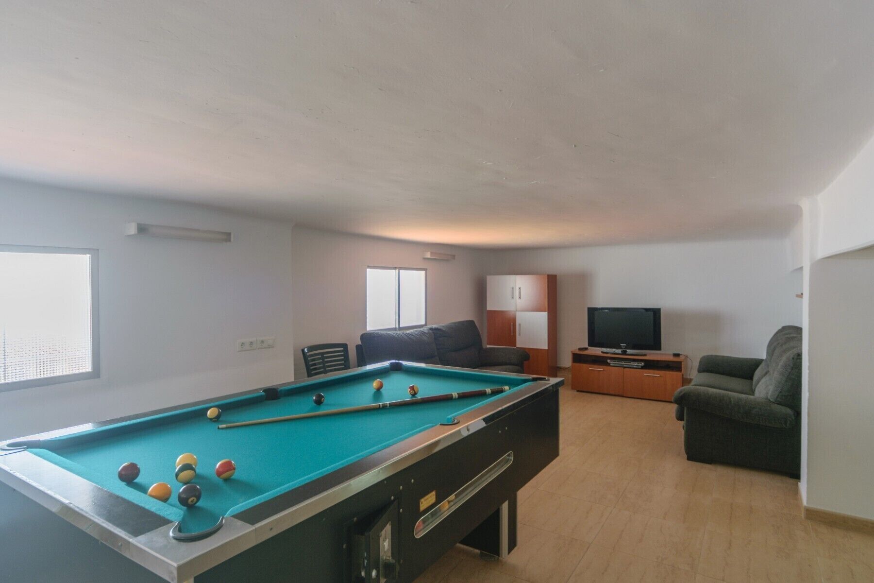 A pool table with balls, a sofa, a television, and a cabinet in a room with a sloped ceiling.