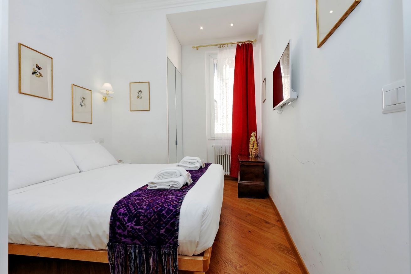 Une chambre à coucher avec un lit, une table de chevet, un miroir et des tableaux encadrés accrochés au mur.