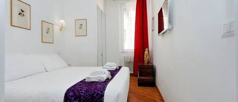 Une chambre à coucher avec un lit, une table de chevet, un miroir et des tableaux encadrés accrochés au mur.