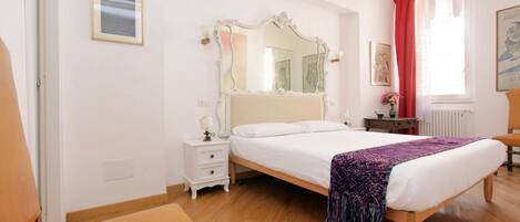 A bedroom with a bed, a nightstand, a chair, a mirror, and a window with curtains.