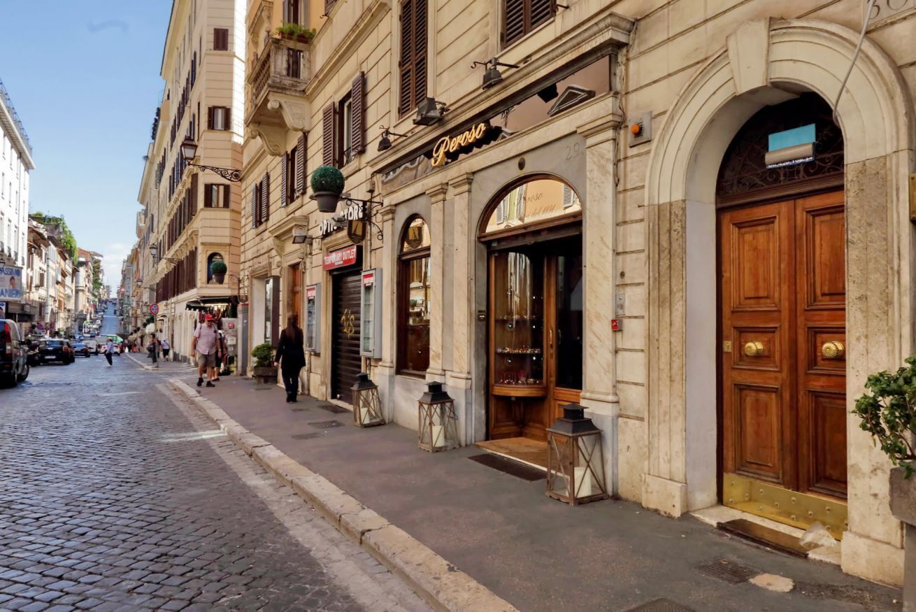 A cobblestone street with historic buildings, a shop named 'Penrose,' and a closed storefront.