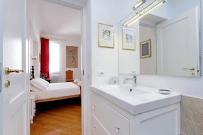 Ein Hotelzimmer mit Bett, einem Badezimmer mit Waschbecken und Spiegel sowie einer Tür zu einem anderen Raum.