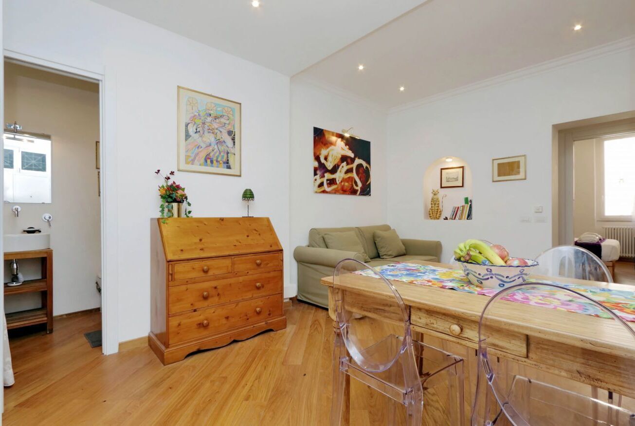 A room with a wooden dresser, a sofa, a dining table with chairs, and artwork on the walls.