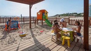 Een kinderspeelplaats aan het strand, met een glijbaan, een klein speelhuisje en een tafel met stoelen.