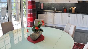 Una cucina moderna con mobili bianchi, un piano di lavoro nero e un tavolo da pranzo in vetro con un sottopiattino rosso.