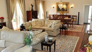 Un ampio soggiorno con un divano color beige, un tavolino da caffè e un'area pranzo illuminata da un lampadario.