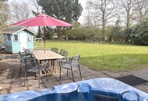 A backyard with a hot tub, a wooden table with chairs, a small shed, and a swing set.