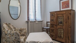 Un dormitorio con cama, un armario de madera, una silla, un radiador y una ventana con cortinas.