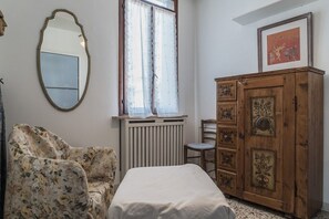 A bedroom with a bed, a wooden cabinet, a chair, a radiator, and a window with curtains. - Three Terraces (Venezia)