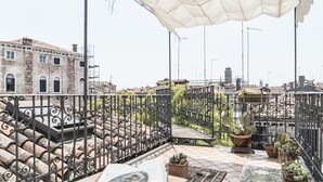 Una terraza en la azotea con mesa, sillas y plantas en macetas.