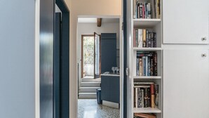 Un pasillo que conduce a una cocina con una escalera, una estantería llena de libros y una puerta que da a otra habitación.