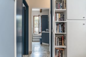 A hallway leading to a kitchen with a staircase, a bookshelf filled with books, and a door leading to another room. - Three Terraces (Venezia)