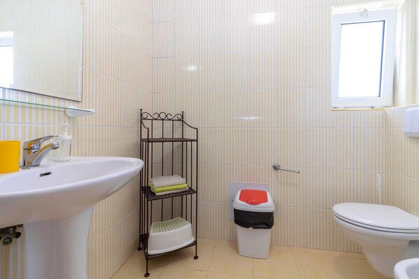Une salle de bain équipée d’un lavabo, de toilettes et d’une étagère en métal.