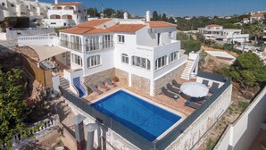 Eine große, weiße Villa mit Swimmingpool, mehreren Balkonen und Blick auf die umliegende Nachbarschaft.