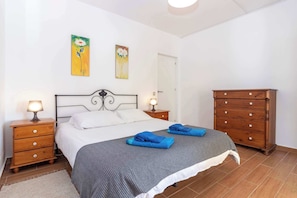 A bedroom with a bed, two nightstands with lamps, a wooden dresser, and two wall-mounted paintings.