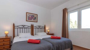 Ein Schlafzimmer mit zwei Betten, Holz-Kopfteilen, Nachttischlampen, einem gerahmten Bild an der Wand und einem Fenster mit Vorhängen.