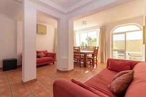 A living room with a sofa, a dining table with chairs, and a TV mounted on the wall.