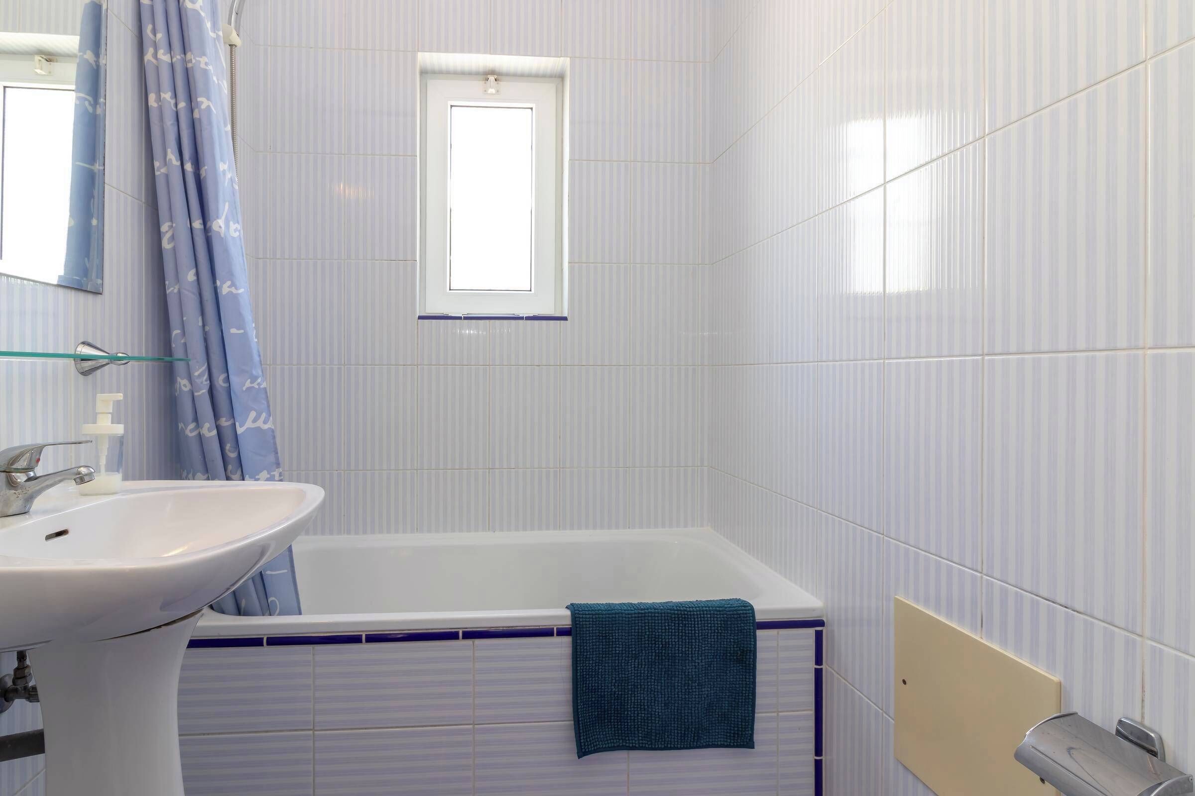 Ein Badezimmer mit einem weißen Waschbecken, einer Badewanne, einem Fenster und einem Handtuch, das an der Wanne hängt.